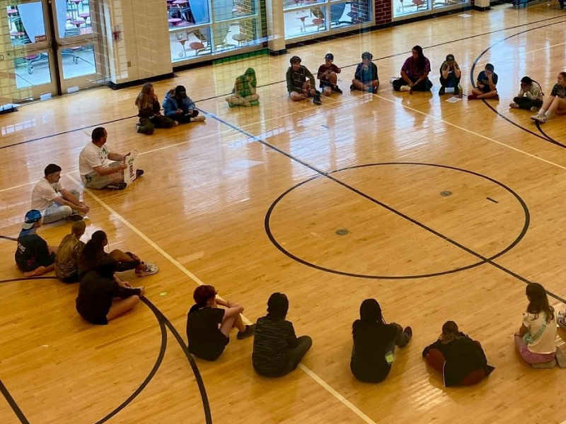 A group of children form a circle on a gym floor