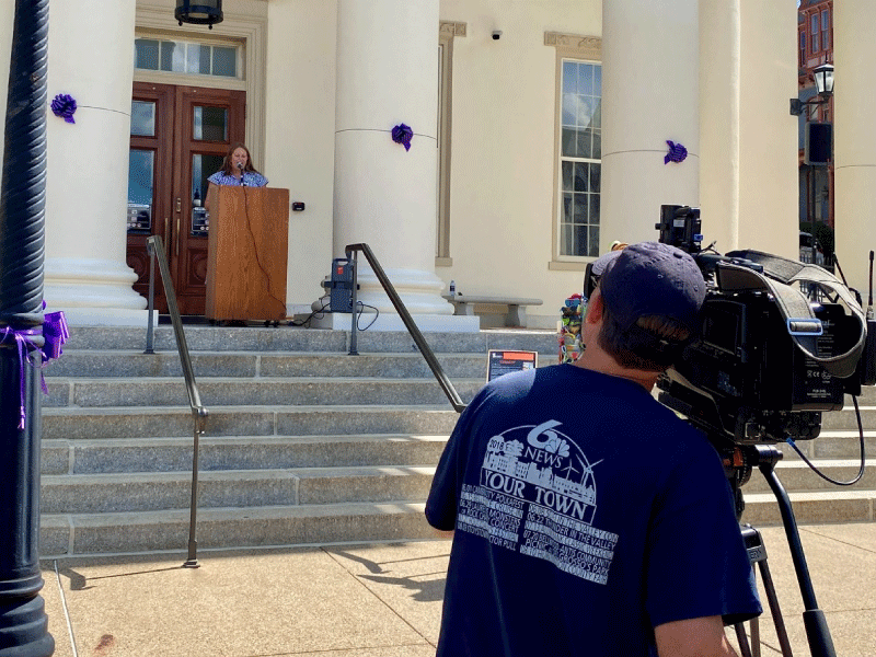 A television camera records JMF staff speaking in front of the court house
