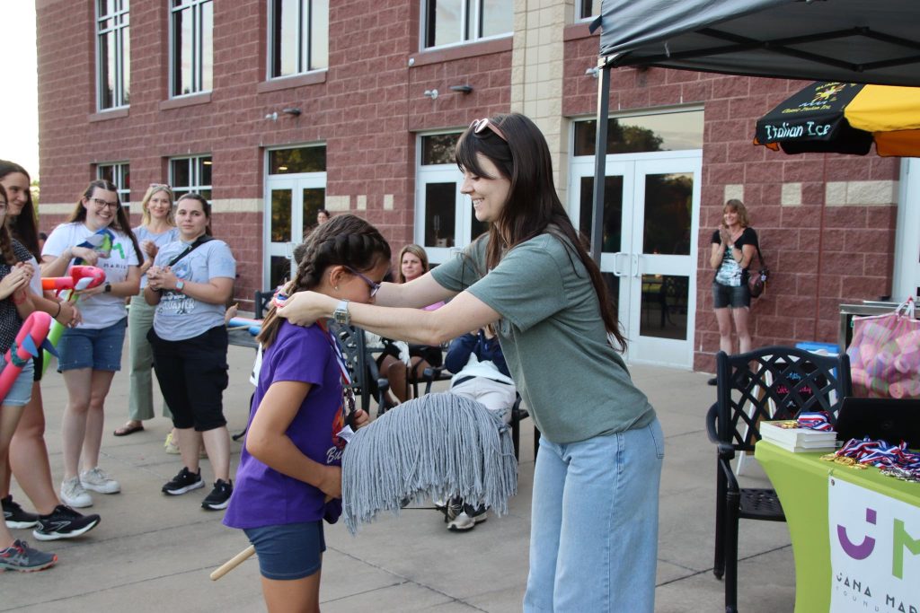 A Jana Marie Foundation staff person awards a ribbon to a winner of the hobby horse derby