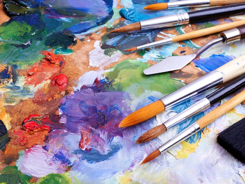 Paintbrushes rest on an abstract painting of flowers