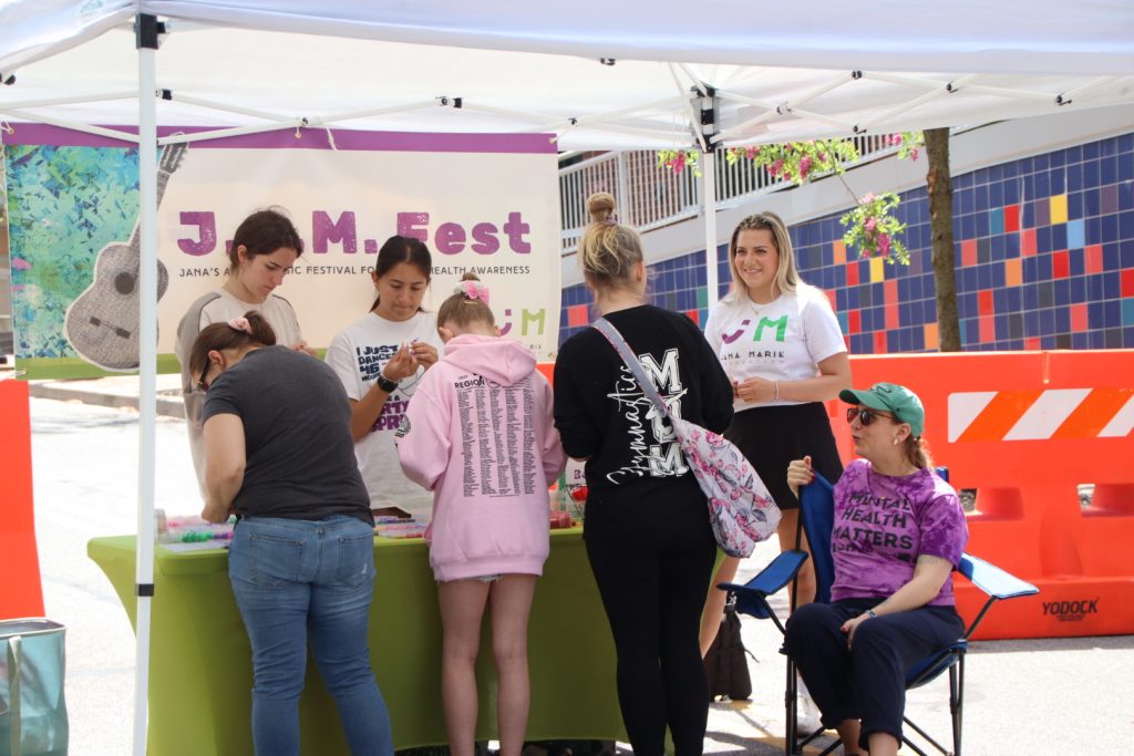 people making beaded bracelets at an outdoor table at a street festival